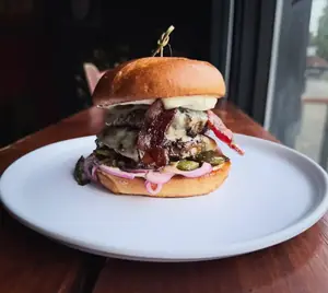 A tall burger with bacon and red onions on a Hawaiian bun