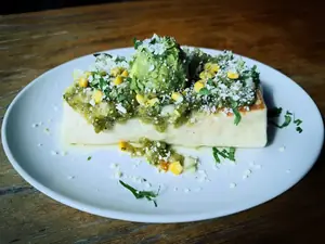 A burrito topped with verde salsa, corn, guacamole and crumbled cotija