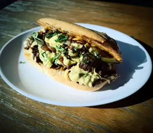 A vegan Philly on a torta roll, piled with chunk steak, peppers, onions and queso